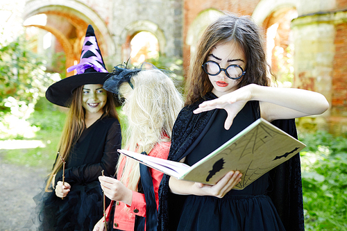 Halloween girl with open spell book doing witchcraft with her friends on background