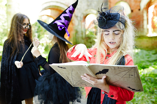 Cute girl in halloween attire looking through spell book and choosing magic-spell