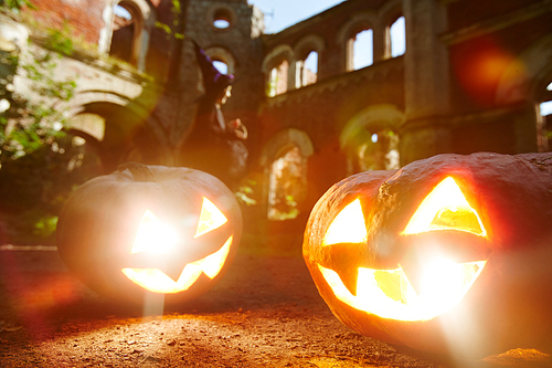 Scary smiles and eyes of jack-o-lanterns on background of ruined structure