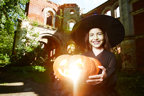 Happy girl in hat and black attire holding jack-o-lantern and