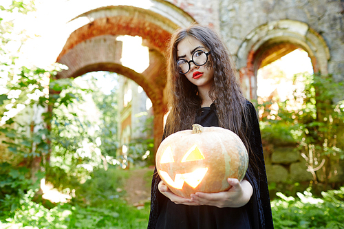 Little girl in black warlock and eyeglasses holding halloween pumpkin