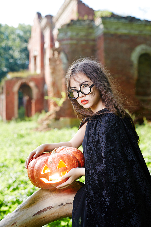Gloomy halloween girl in black warlock holding jack-o-lantern