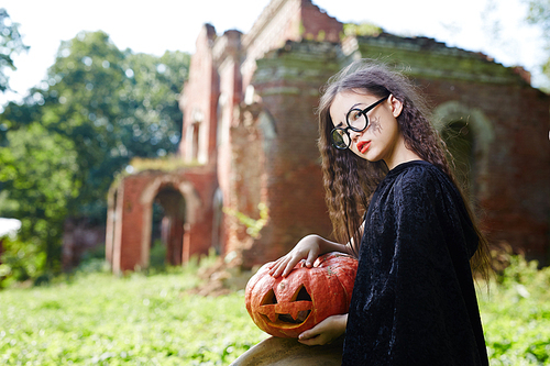 Little witch with halloween pumpkin sitting in natural environment