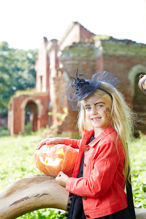 pretty little witch with jack-o-lantern looking at camer in natural