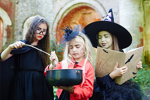 Little halloween witches with spell-book and magic stick preparing potion for tricks