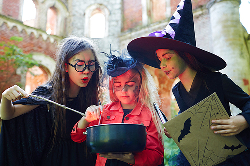Gloomy halloween witches saying black magic spells over pot with poisonous brew