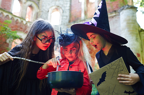 Astonished halloween girls looking into pot with witch-brew