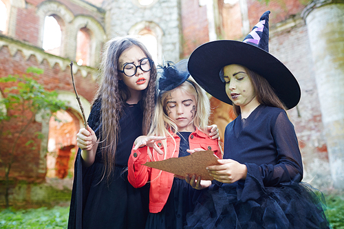 Little girls in witch attire reading halloween spell on paper
