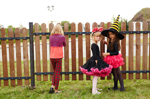 three little girls in halloween costumes standing by fence in rural