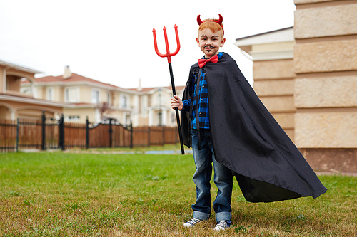 Boy in warlock holding trident and  while standing on grass by corner of house