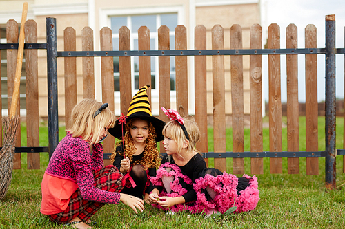 Three girls in traditional halloween costumes playing in the yard by fence