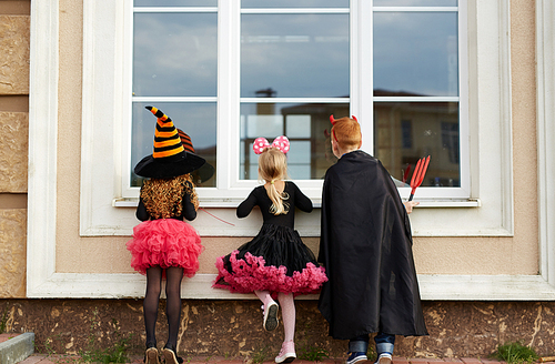 Halloween boy and girls looking through window of house from outside