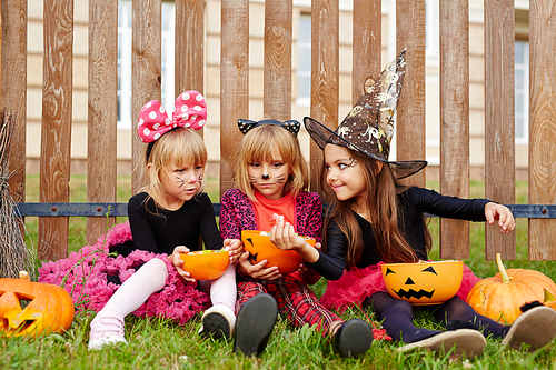 Halloween girl showing tasty treat to her friends while eating candies