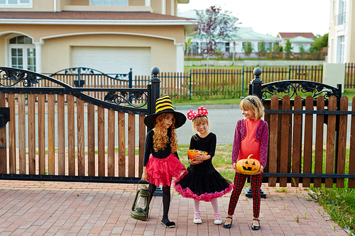 Trick-or-treat girls standing by fence of house they visited