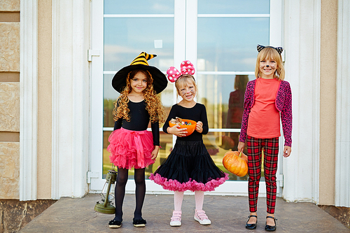 Happy youthful girls with halloween treats standing by door of house