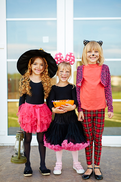 Cute halloween girls with treats standing by door outside