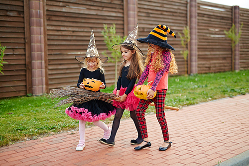 Little halloween witches in hats moving down pavement during trick-or-treat promenade