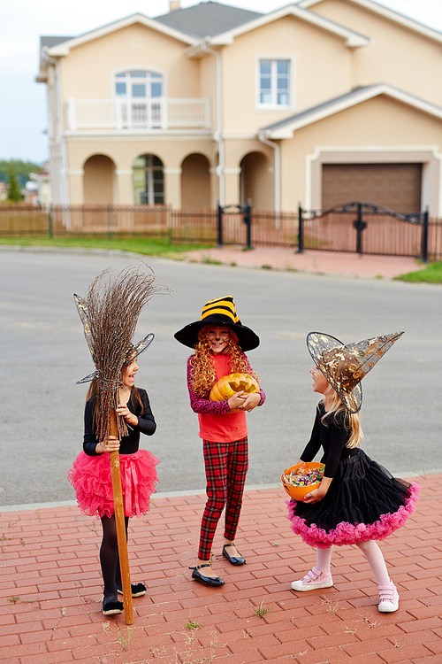 Three halloween characters with broom, treat candies and pumpkin having talk outdoors