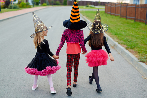 Little girls in witch costumes and hats walking away after halloween tricks