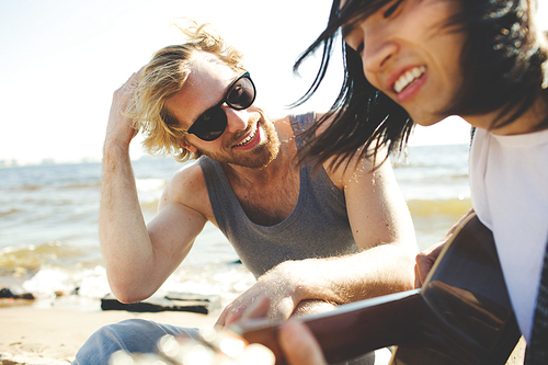 Happy guys with guitar enjoying summer vacation on the beach