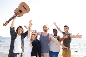 Ecstatic young people with guitar raising their hands on background of water