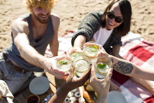 Young people toasting with glasses of mojito cocktail at beach party
