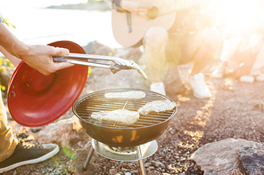 Young man preparing grilled steak for friends at picnic