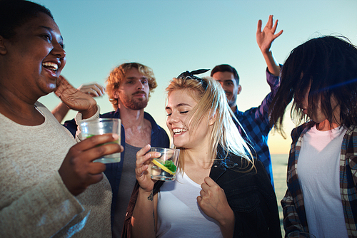 Cheerful friends with drinks dancing outdoors in summer