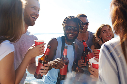 Large group of buddies with drinks spending leisure by seaside