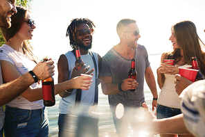 Happy guys and girls with drinks enjoying time by seaside