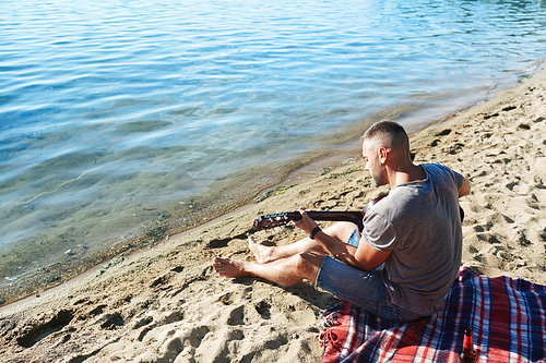 Young man playing guitar while relaxing on sandy beach