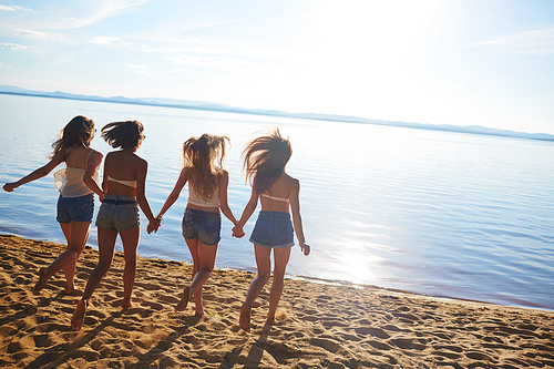 Group of carefree girls running towards water for refreshment