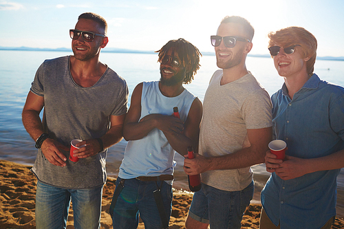 Multi-ethnic group of guys in sunglasses enjoying beach party