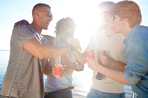Ecstatic guys with drinks enjoying sunny day on the beach