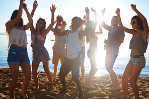 Group of ecstatic guys and girls ancing on sand