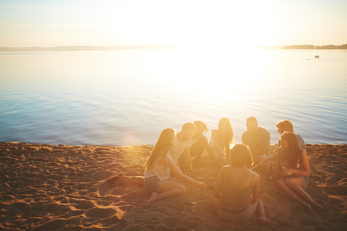 Several teenagers gathered around campfire by seaside