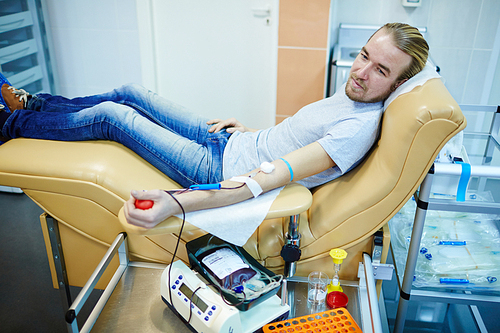 Young selfless man transfusing his blood in center of voluntary blood-drive