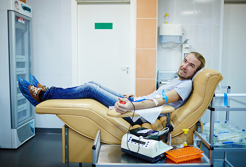 Young donor of blood sitting in armchair in hemotransfusion station