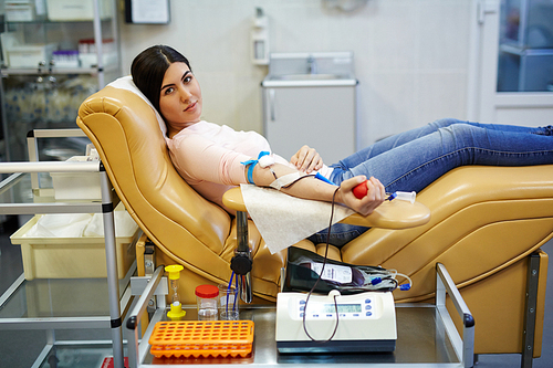 Donor of blood gripping special flexor while sitting in armchair