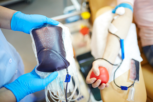 Human hands in gloves holding blood-bag with fresh blood