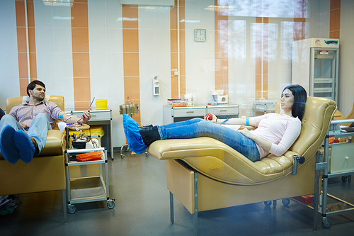 Young donors in shoe-covers lying in armchairs and gripping flexors