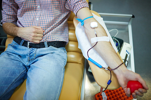 Donor with his arm on armrest lying in armchair and donating blood