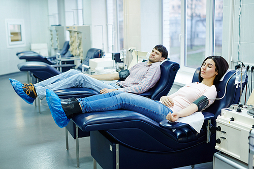 Guy and girl ready for blood transfusion lying in armchairs