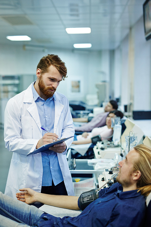 Doctor making notes while talking to young man during hemotransfusion process