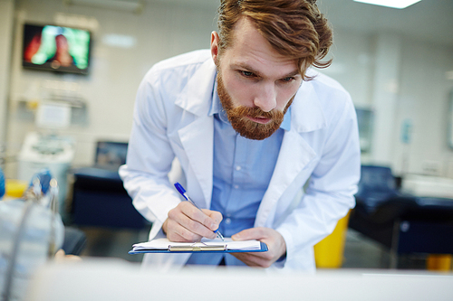 Young clinician rewriting indications from blood transfusion machine