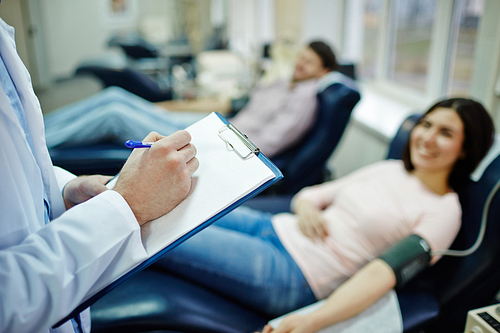 Clinician with blank paper and pen making notes in blood donating center