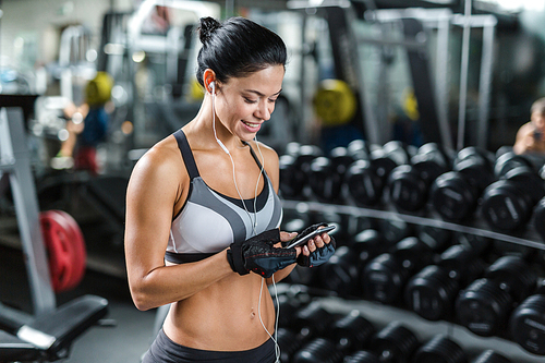 Portrait of well-built muscular woman listening to music using smartphone in gym before working out