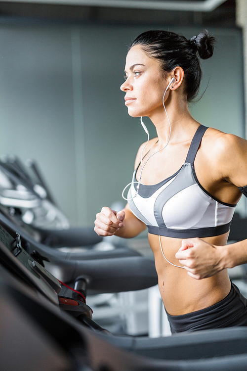 Close view portrait of sportive brunette woman  running on treadmill in gym listening to music using shoulder smartphone holder