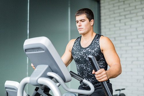 Portrait of muscular sportive man  running using elliptical trainer during workout in modern gym
