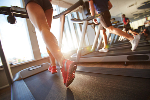 Low-angle view of male and female legs running on treadmill in gym on sunny day